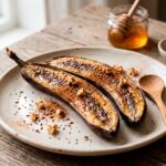 Sobremesa de banana assada fitness com canela em pó servida em um prato branco, ideal para pré-treino.